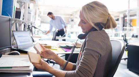 A woman talking on her office phone while reviewing her notes.